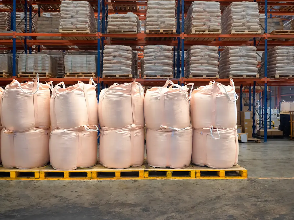 Insumos agrícolas organizados dentro de bags, sobre pallets de madeira amarelos em galpão