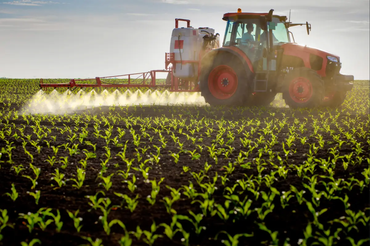 Trator fazendo uma pulverização agrícola na lavoura.